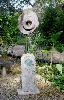Ancient wagon wheel with stone cross in copper rising from fossil stone.
6' tall garden piece.